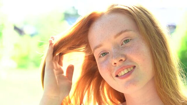 The face of a beautiful red-haired girl in backlight. Portrait a smiling young woman with red hair and freckles against the backdrop of a bright sunny meadow. Natural beauty with freckles