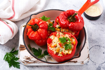 Red bell peppers stuffed with rice and vegetables on cast iron pan on gray concret background