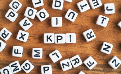 Small white and black bead cubes on wooden board, letters in middle spell KPI - Key Performance Indicators concept