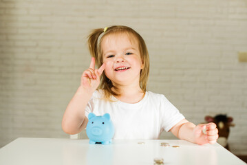Little cute and emotional blonde girl with piggy bank. The child manages and deposits his finance, girl saving money in a piggybank for future. 