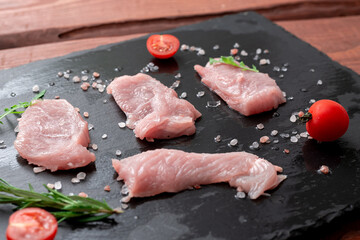 Raw turkey fillet on a black stone background with rosemary and coarse salt.