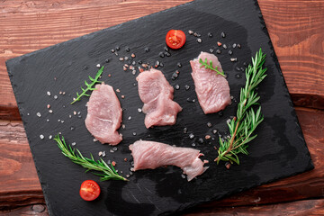 Raw turkey fillet on a black stone background with rosemary and coarse salt.