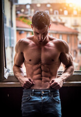 Fototapeta premium Sexy shirtless muscular young man next to window, wearing only jeans, looking out