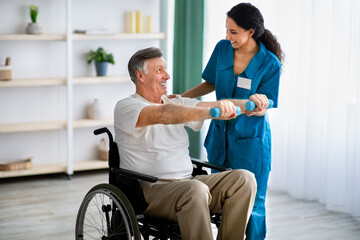 Female physiotherapist helping elderly man in wheelchair do exercises with dumbbells at health...