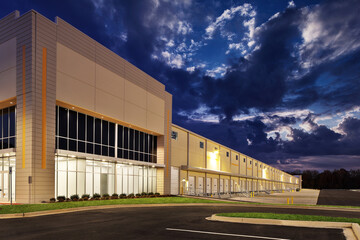 Large lit generic white industrial storage warehouse façade at night dusk