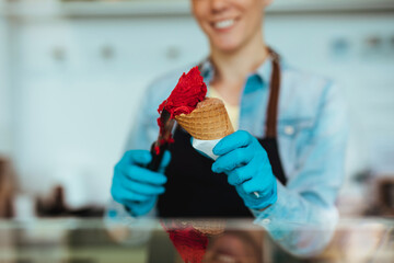 Close up of saleswoman in black apron selling handmade ice cream at the counter of the pastry shop.