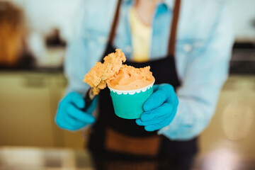 Close up of saleswoman in black apron selling handmade ice cream at the counter of the pastry shop.