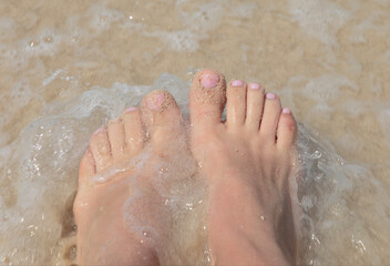 women's feet are washed by the surf on the sand