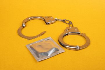 handcuffs and condoms on yellow background, illegal sex prostitution.