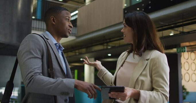 Diverse businessman and businesswoman talking and using tablet in lobby of modern office