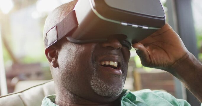 Happy african american senior man sitting in sunny living room using vr headset and smiling