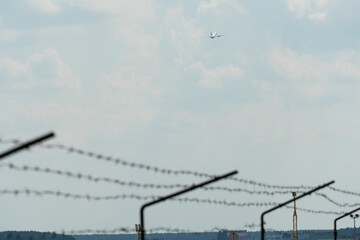 Barbed wire on a background of blue sky and white clouds and a plane taking off. Dictatorship in...