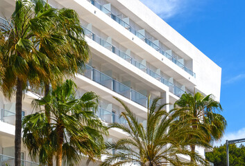 Facade of a hotel with balconies and palm trees in the foreground in a holiday resort