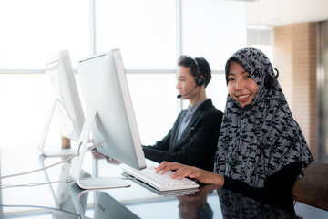 Smiling Young beautiful Muslim women in hijab and businessmen wearing microphone headsets is working as customer care operator or help desk service and team support information in call center office.