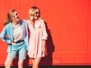 Two young beautiful smiling hipster female in trendy summer  clothes.Sexy carefree women posing on street background near red colorful wall.Positive models having fun and hugging. Cheerful and happy