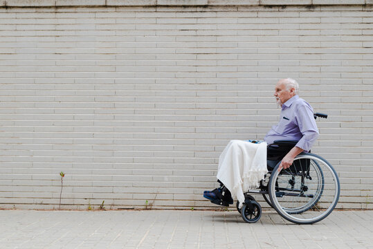 Elderly Man In Wheelchair Riding Along Street