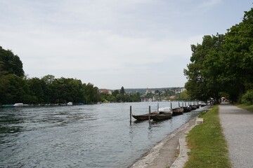 Fototapeta na wymiar Promenade along Rhine river in Schaffhausen, Switzerland. There are wooden boats moored along the river bank. They are called weidling boot in German language and they are traditional Swiss boats.