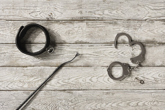 Handschellen, Peitsche und Halsband auf einem alten Brett liegend