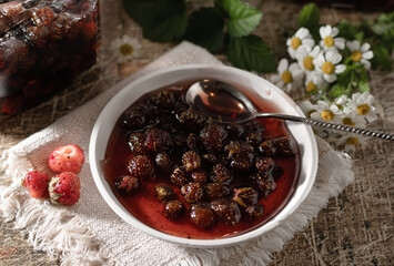 Wild strawberry jam in a white small plate and daisies on a rustic background. Homemade strawberry marmalade and fruit. Selective focus.