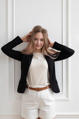 Young beautiful Caucasian woman in casual office clothes standing and touching her hair, posing, looking at camera. Vertical shot.