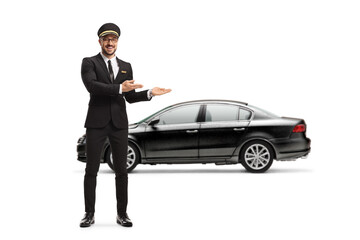 Full length portrait of a professional chauffeur pointing at a black car - obrazy, fototapety, plakaty