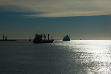 Silhouettes of cargo ships leaving the bay to the sea, accompanied by a tug, at sunset.