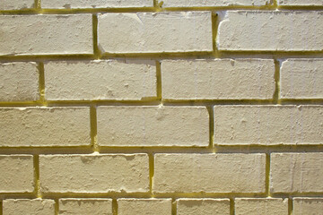 Frontal view of a yellow old brick wall with harsh shadows. The bricks are mortar-bonded and...