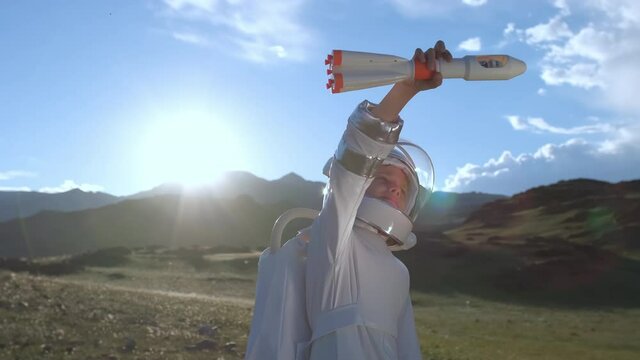 Little young happy child boy wearing astronaut uniform and helmet cosmonaut playing with toy rocket at sunset. Space man, Kid big dream flying, childhood, freedom, travel, future, professions concept