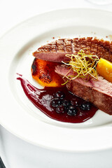 Red meat sous vide steak with peaches i, berry and red wine sauce, served on a white porcelain plate
