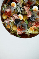 Classic nicoise in the author's serving tuna salad with fresh vegetables on a white napkin, canned tuna with masilnas, onions and eggs, top view, copy space