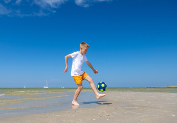Happy teen boy playing with ball on beach at summer sunny day with blue sky