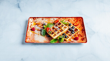 Closeup of the sweet and delicious waffles covered in syrup and fruits on the plate..