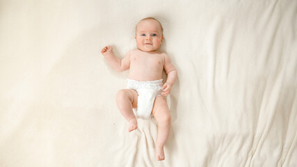 Top view of little baby boy in diapers lying on soft white blanket on bed.