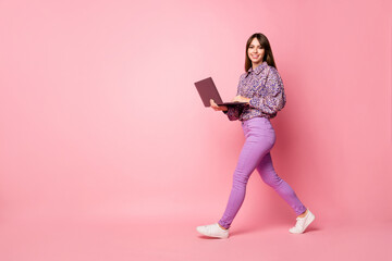 Full length profile photo of cheerful charming person walking hands hold laptop isolated on pink color background