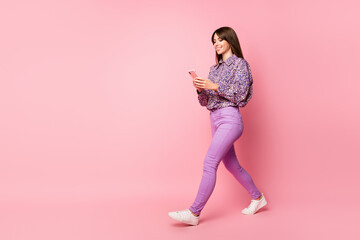 Full size profile side photo of young happy cheerful smiling girl go walk using smartphone isolated on pink color background