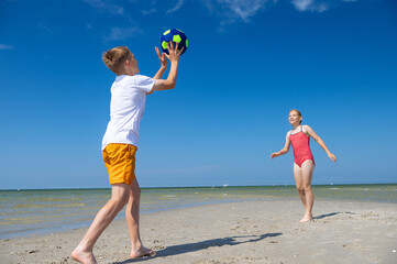 Happy children playing with ball on beach at summer sunny day with blue sky