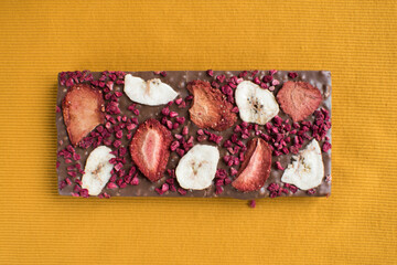 a bar of delicious milk chocolate with additions of dry raspberries and banana chips in place for the text in a bright yellow color