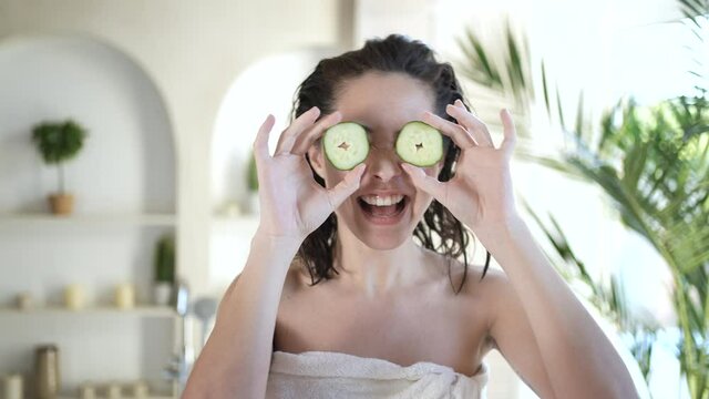 Funny asian woman covering eyes with cucumbers fresh clean healthy skin care concept. Cute mixed race girl holding organic vegetable during beauty treatment therapy enjoy daily bodycare in bathroom
