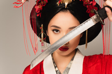 Japanese woman in national costume holding blurred sword near face isolated on grey