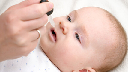Closeup of little baby boy taking vitamin D from eyedropper. Concept of newborn healthcare and...