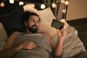 Young man with phone in bed in the evening. Evening leisure at home © Anna