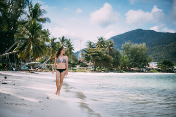 Beautiful woman in a swimsuit walks on a tropical beach