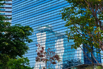 Obraz na płótnie Canvas High-rise building glass wall mirroring part of Marina Bay Sands, Singapore. Reflections, sunlight, green trees. Iconic tourist destination, must-see