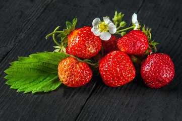 Ripe red strawberries with leaves and flowers on a black vintage table. Summer sweet diet and healthy vitamin pack