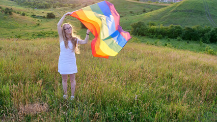 Bisexual, lesbian, woman, person, homosexual holds LGBT flag on the green hills on a sunny day sunset and celebrating a gay parade, Bisexuality Day or National Coming Out Day in pride month