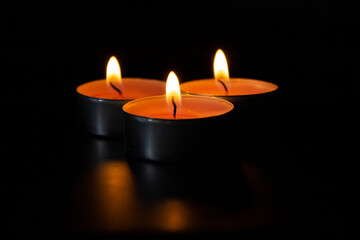 Dark night background, composition of three candles. Black table, side view. Candles Burning at Night. Orange taper burning in focus, foreground. illustration design.