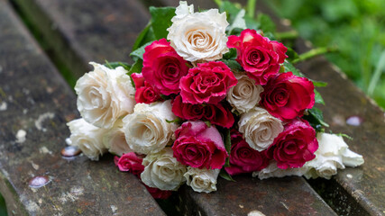 Bouquet of roses, white and pink, abandoned on a wooden bench, in the middle of a park, on a rainy day, close up