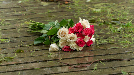 Bouquet of roses, white and pink, thrown over the wooden bridge to the lake on a rainy day

