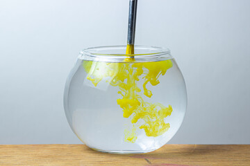 A paintbrush with yellow paint is dipped in a jar of water on a white background. The paint spreads in the water. - Powered by Adobe