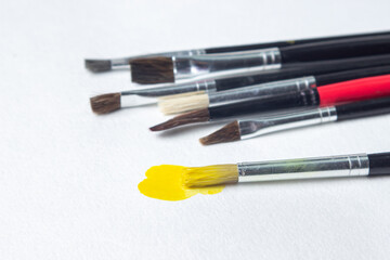 Fototapeta premium Paint brushes on a white background. One brush with yellow paint. Watercolor paint